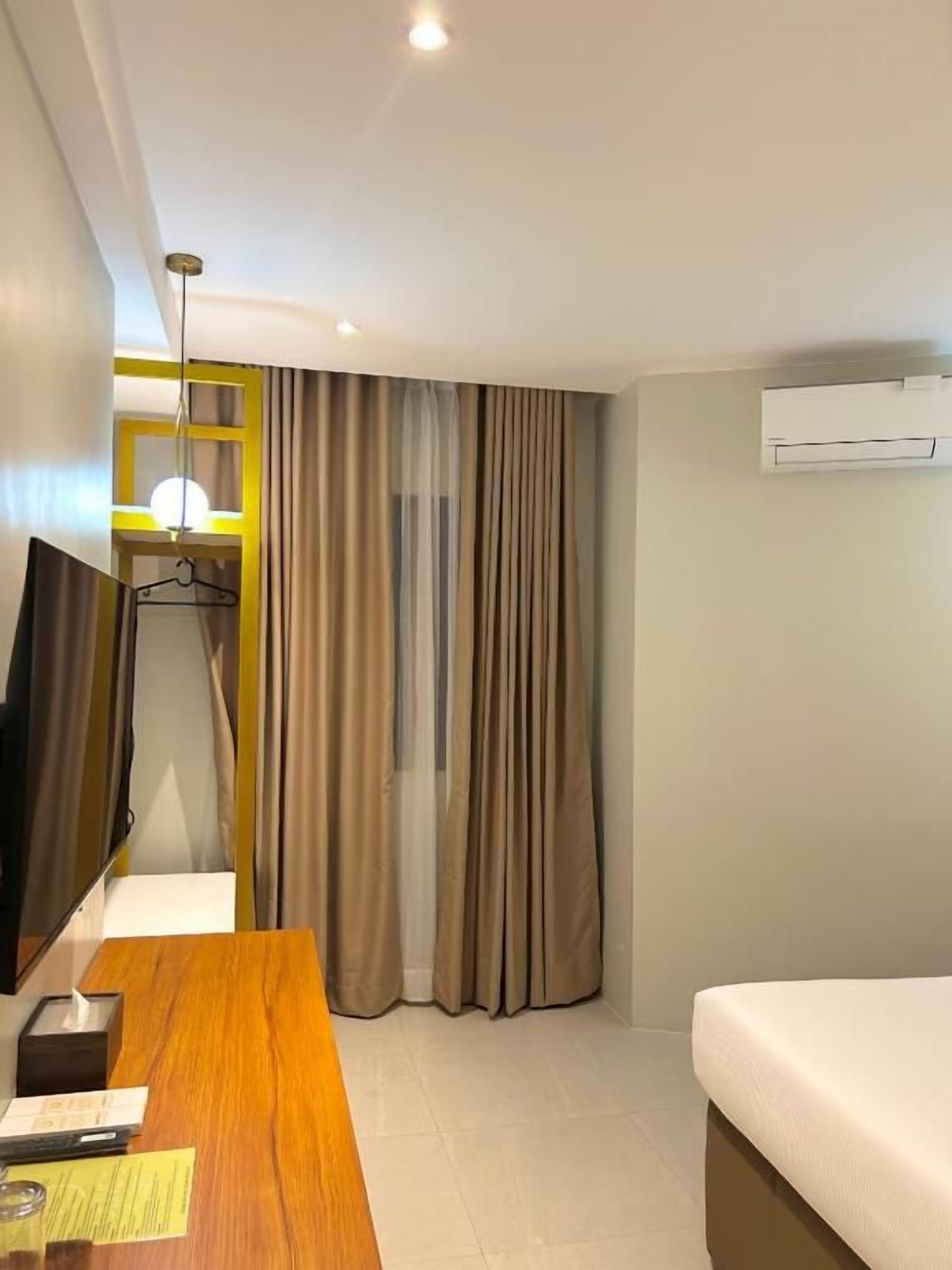 Ein Hotelzimmer mit einem Bett, einem Schreibtisch mit Stuhl, einem Fernseher und einer Klimaanlage.