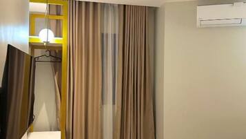 Ein Hotelzimmer mit einem Bett, einem Schreibtisch mit Stuhl, einem Fernseher und einer Klimaanlage.