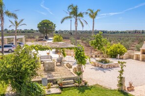 Un patio con mobiliario exterior, una pérgola cubierta de hiedra y vistas a un viñedo al fondo.