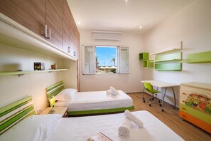 Ein Hotelzimmer mit zwei Betten, einem Schreibtisch, einem Stuhl und einem Fenster mit Blick auf Palmen.