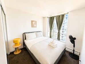 Et hotelværelse med seng, et natbord, en ventilator og et vindue med gardiner.
