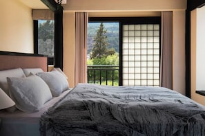 A hotel room with a bed, a view of a balcony, and a window with a view of trees and mountains.
