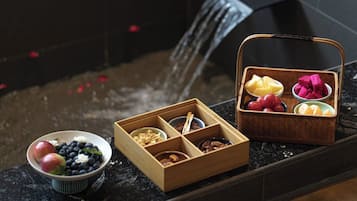 Un plateau en bois, divisé en compartiments, contenant divers fruits, ainsi qu’un bol rempli de pommes et de myrtilles.