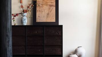 Un mueble de madera oscura con una obra de arte enmarcada encima, dos jarrones de cerámica en el suelo junto al mueble, y un jarrón con ramas sobre el mueble.