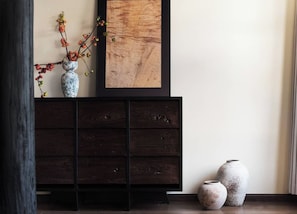 A dark wooden cabinet with a framed artwork above it, two ceramic vases on the floor beside the cabinet, and a vase with branches on the cabinet.