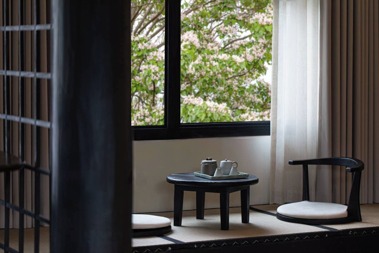 A room with a tatami mat floor, a table with a teapot and cups, and two chairs.