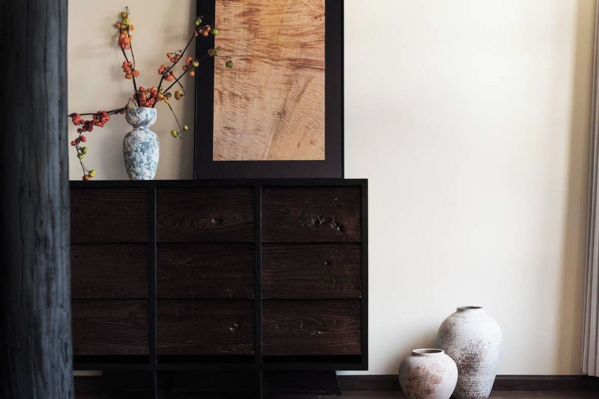 A dark wooden cabinet with a framed artwork above it, two ceramic vases on the floor beside the cabinet, and a vase with branches on the cabinet.
