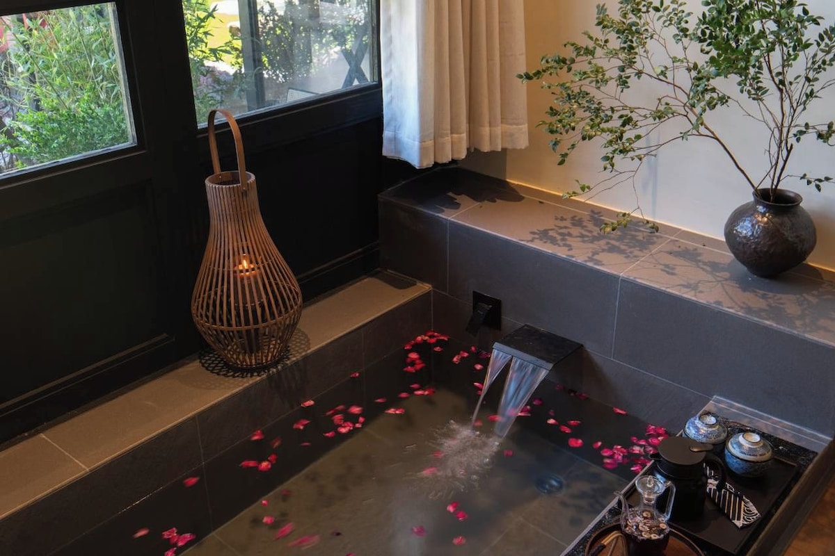 A room with a bathtub, a hanging light fixture, a potted plant, and a tray with a teapot and cup.