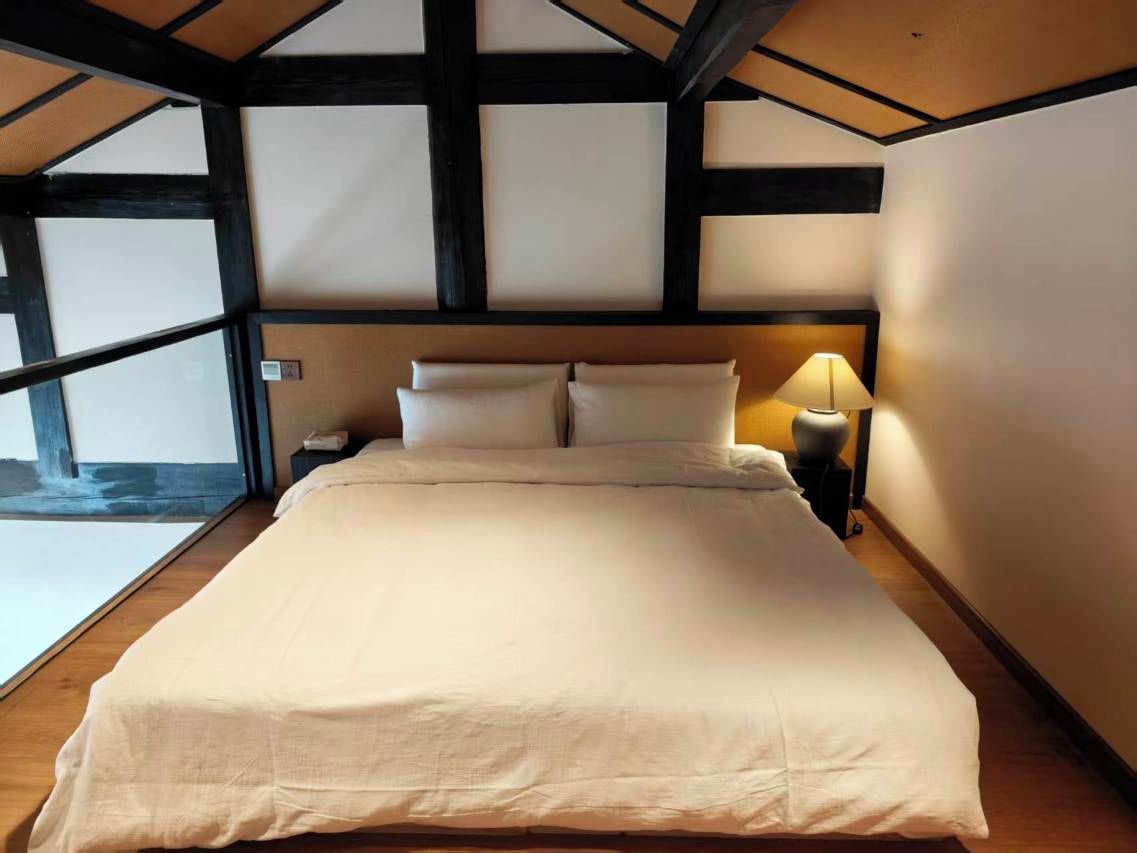 A bedroom with a large bed, a nightstand with a lamp, and a view of a stone wall.