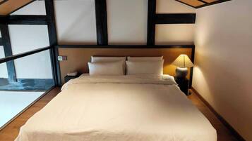 A bedroom with a large bed, a nightstand with a lamp, and a view of a stone wall.