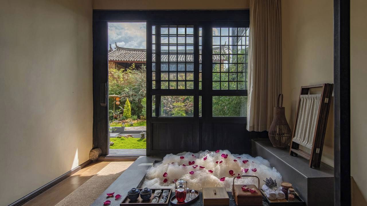 A room with a traditional Japanese sliding door, a tatami mat floor, and a view of a garden with a traditional building.