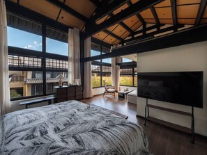 A modern bedroom with a large bed, a flat-screen TV, and a balcony with a view.
