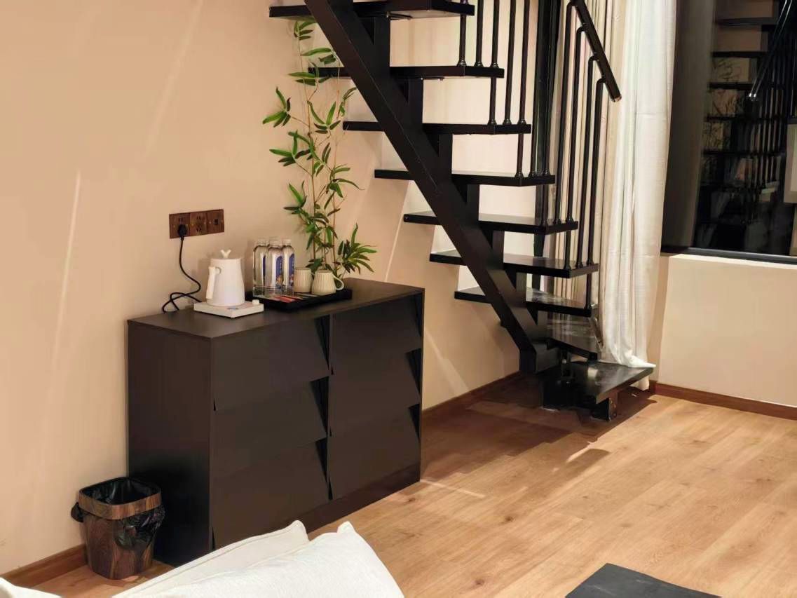 Una habitación con una escalera, un armario, una planta en maceta y un cubo de basura.