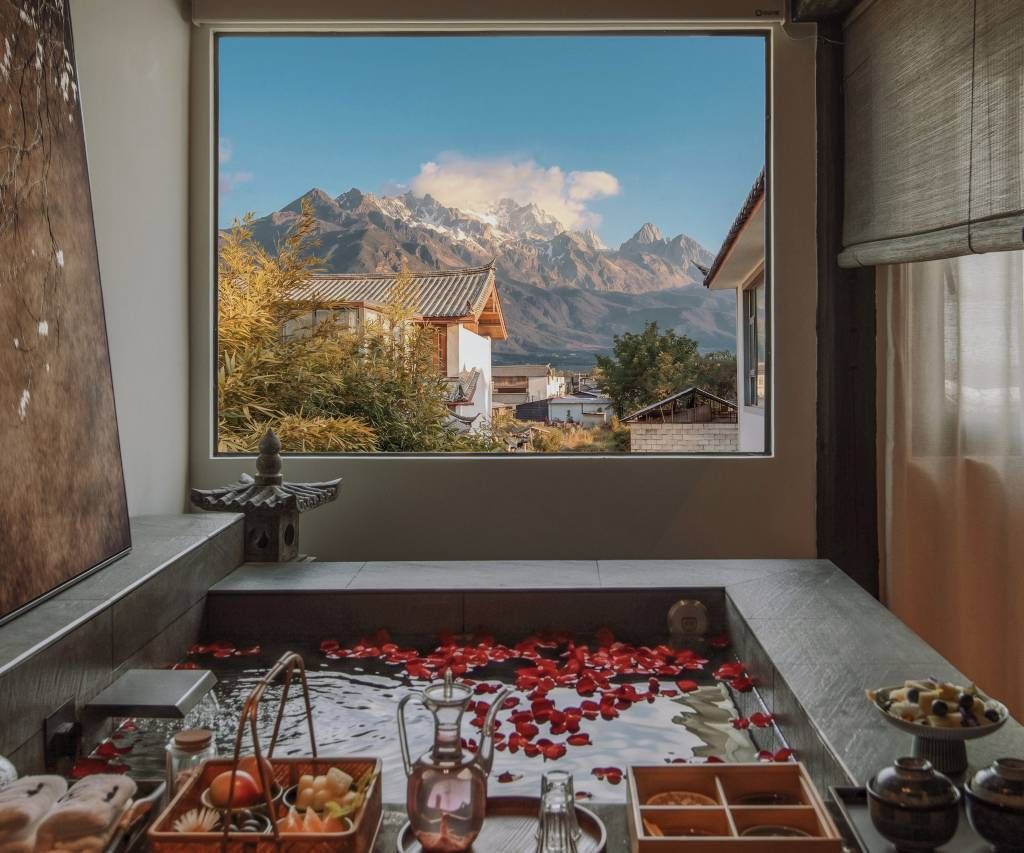 A room with a large window overlooking a mountainous landscape, a traditional Japanese-style water feature, and a table with various items.
