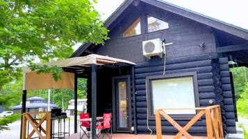 A log cabin with a wooden deck, a covered seating area, and a large window.
