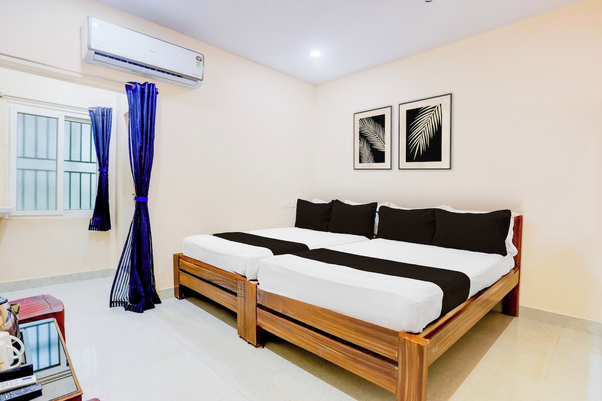 Un dormitorio con cama, equipo de aire acondicionado, cortinas y dos diseños de hojas enmarcadas en la pared.