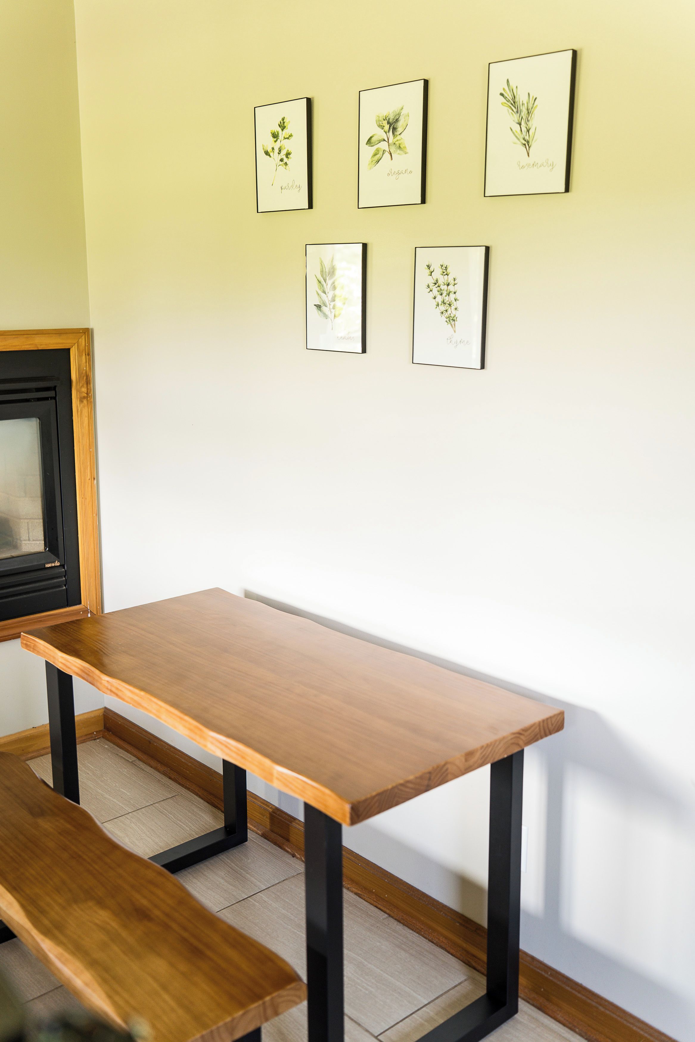 Une pièce avec une table et un banc en bois, un tableau encadré au mur et un objet à cadre noir sur la gauche.