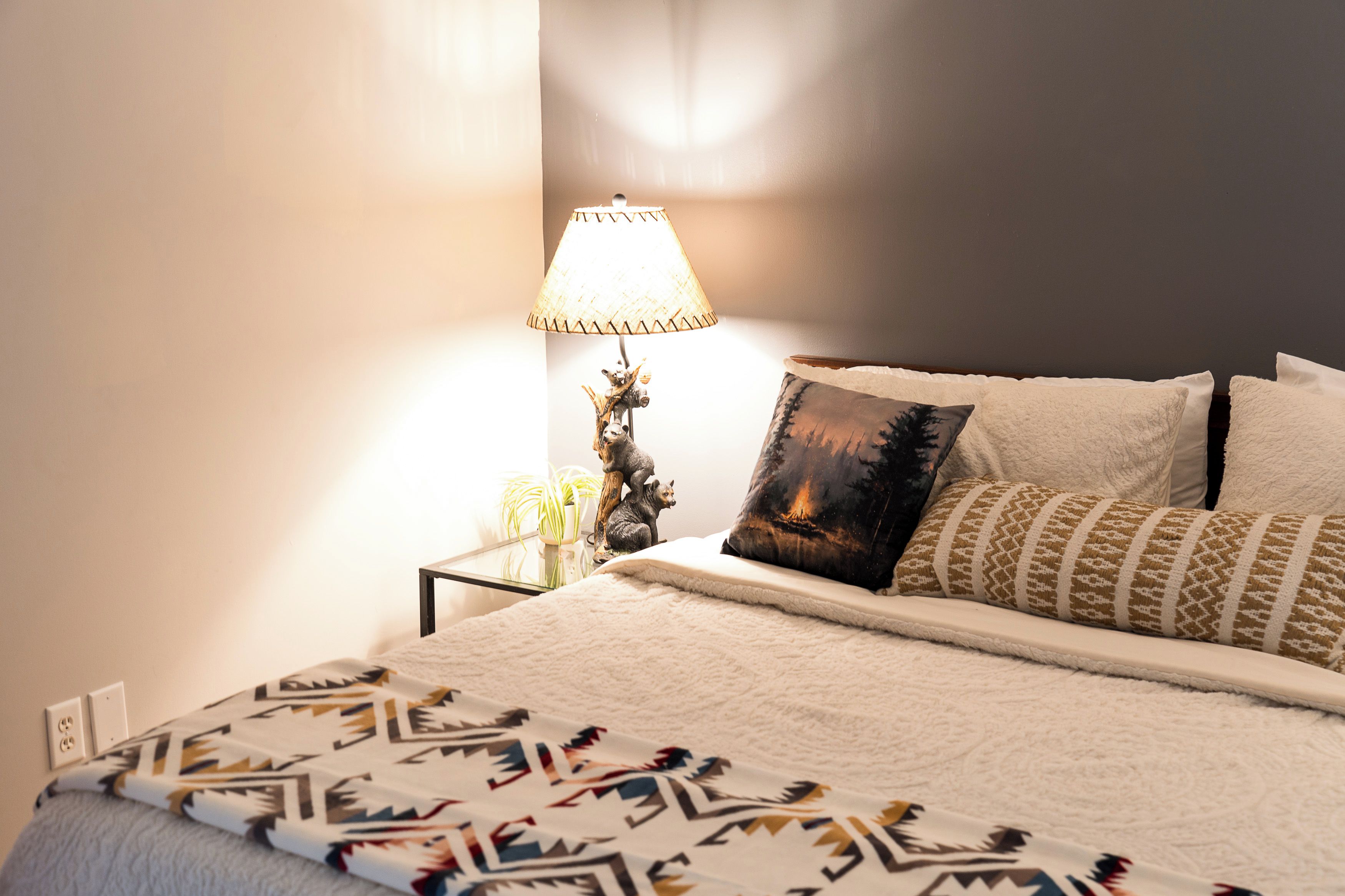 Un lit bien fait, avec une literie à motifs, une lampe de chevet et des coussins décoratifs.