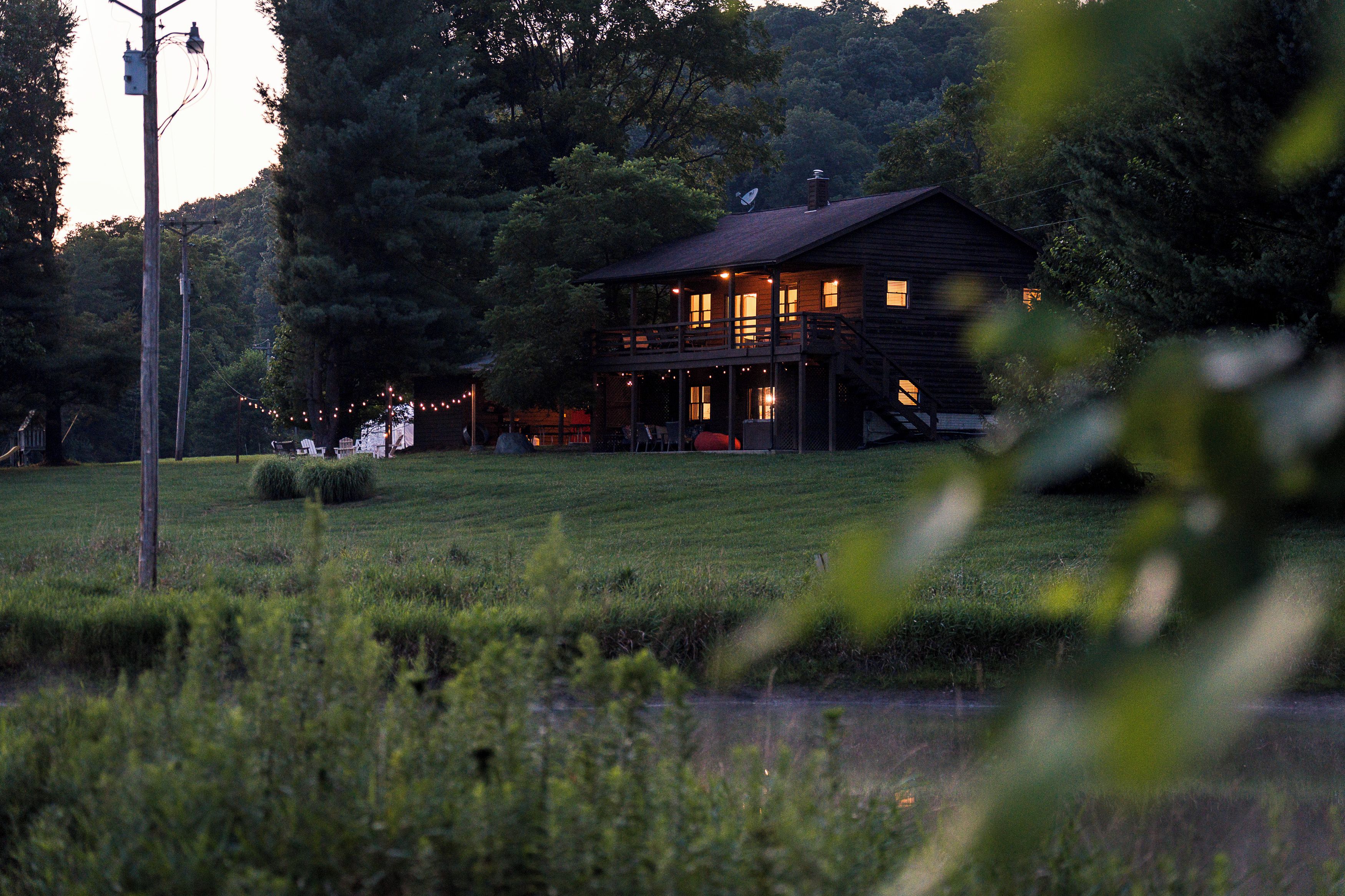 A wooden cabin with a porch, surrounded by trees and a grassy field.
