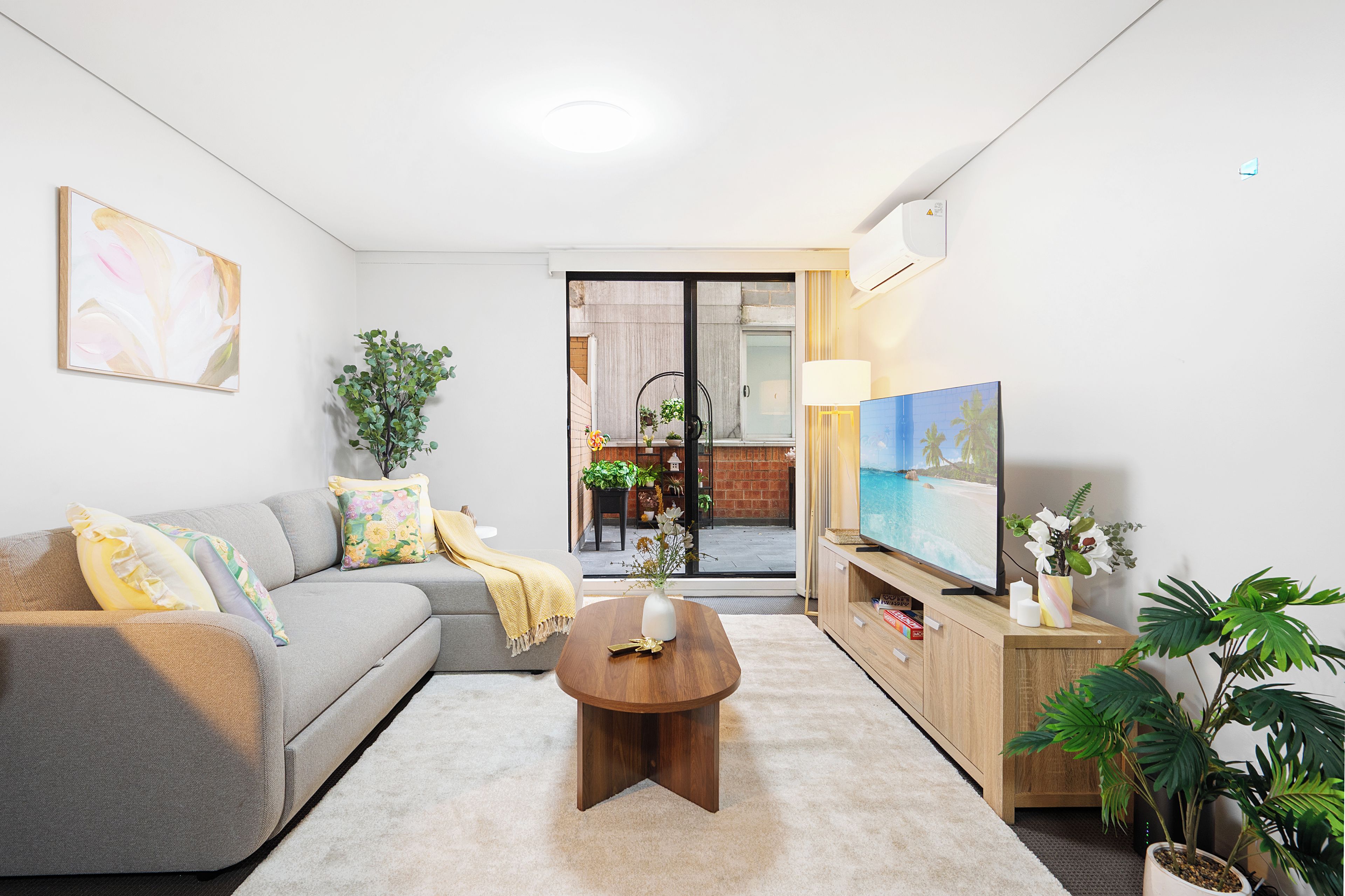 A modern living room with a grey sofa, a wooden coffee table, and a TV on a wooden stand.