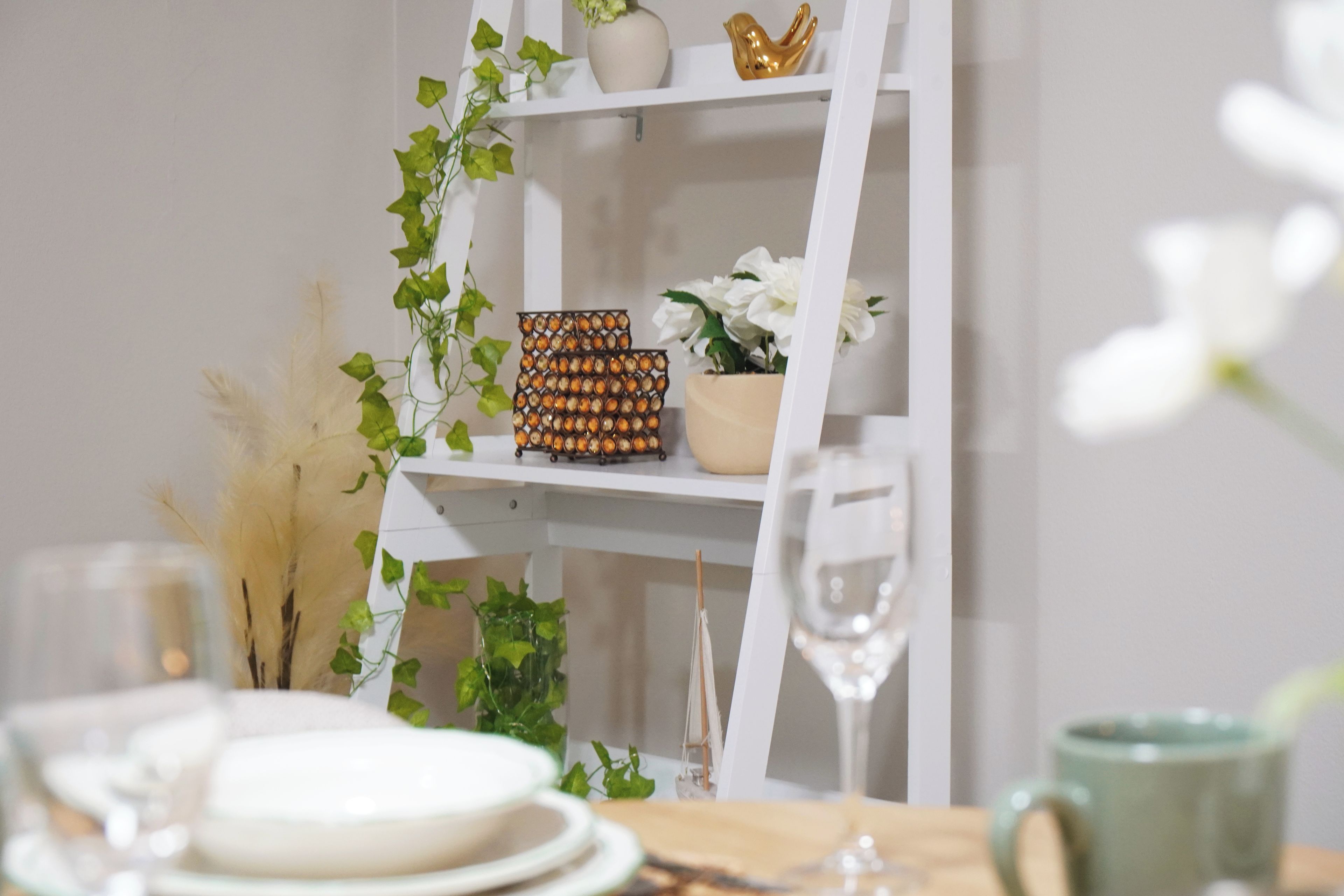A white shelf with decorative items including a golden bird, a potted plant, and a wall-mounted decorative piece.