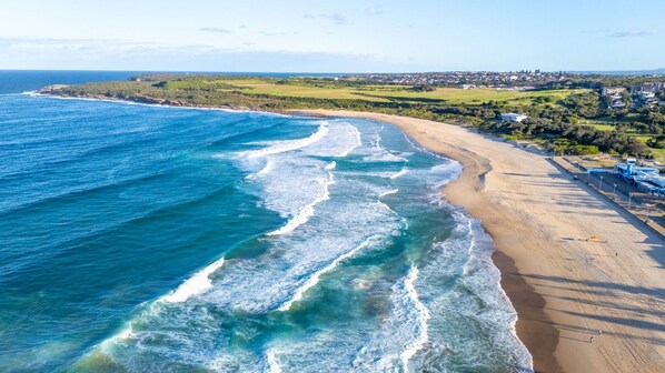 A coastal beach with waves, a sandy shore, and a distant town.
