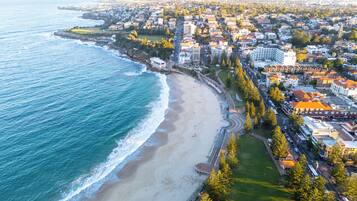 An aerial view of a coastal city with a beach, residential buildings, and a road curving along the shore.