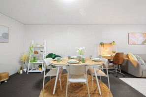 A modern living room with a round dining table, white chairs, a sofa, and a bookshelf.