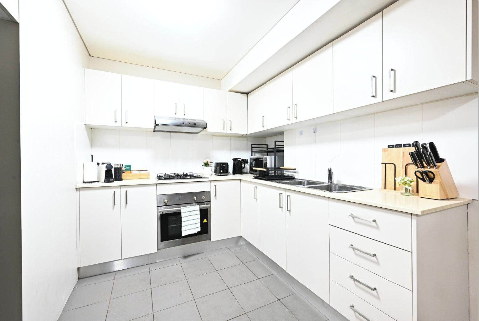 A modern kitchen with white cabinets, a gas stove, a coffee maker, and a knife block.