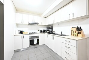 Una cocina moderna con armarios blancos, una estufa a gas, una cafetera y un bloque de cuchillos.