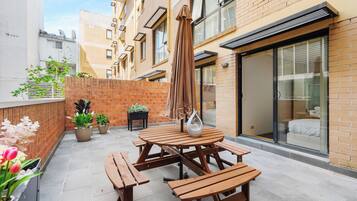 A patio with wooden tables and benches, potted plants, and a sliding glass door leading to a bedroom.