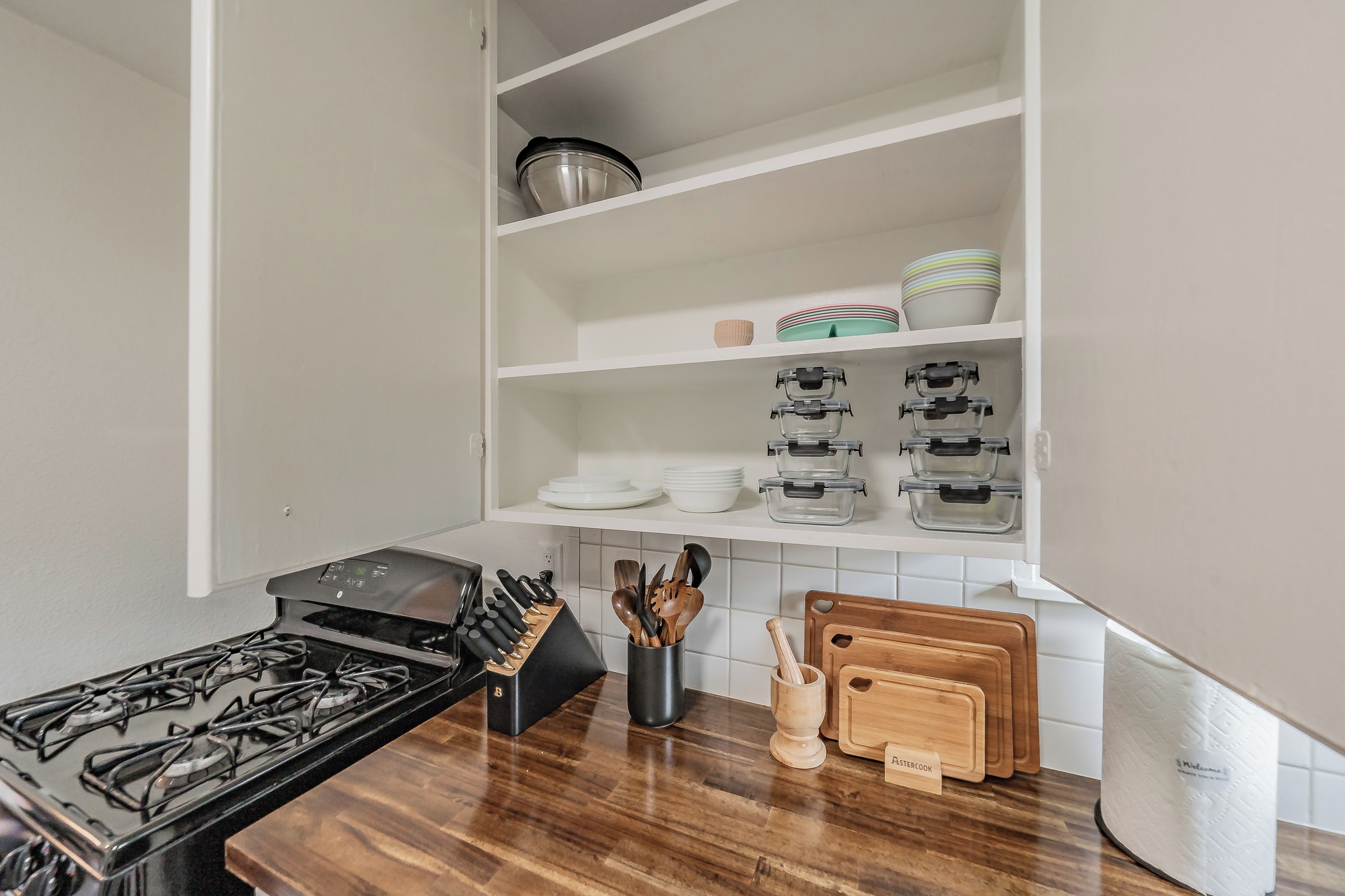 A kitchen with a gas stove, knife block, cutting board, and storage shelves.