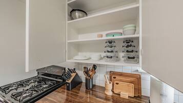 A kitchen with a gas stove, knife block, cutting board, and storage shelves.