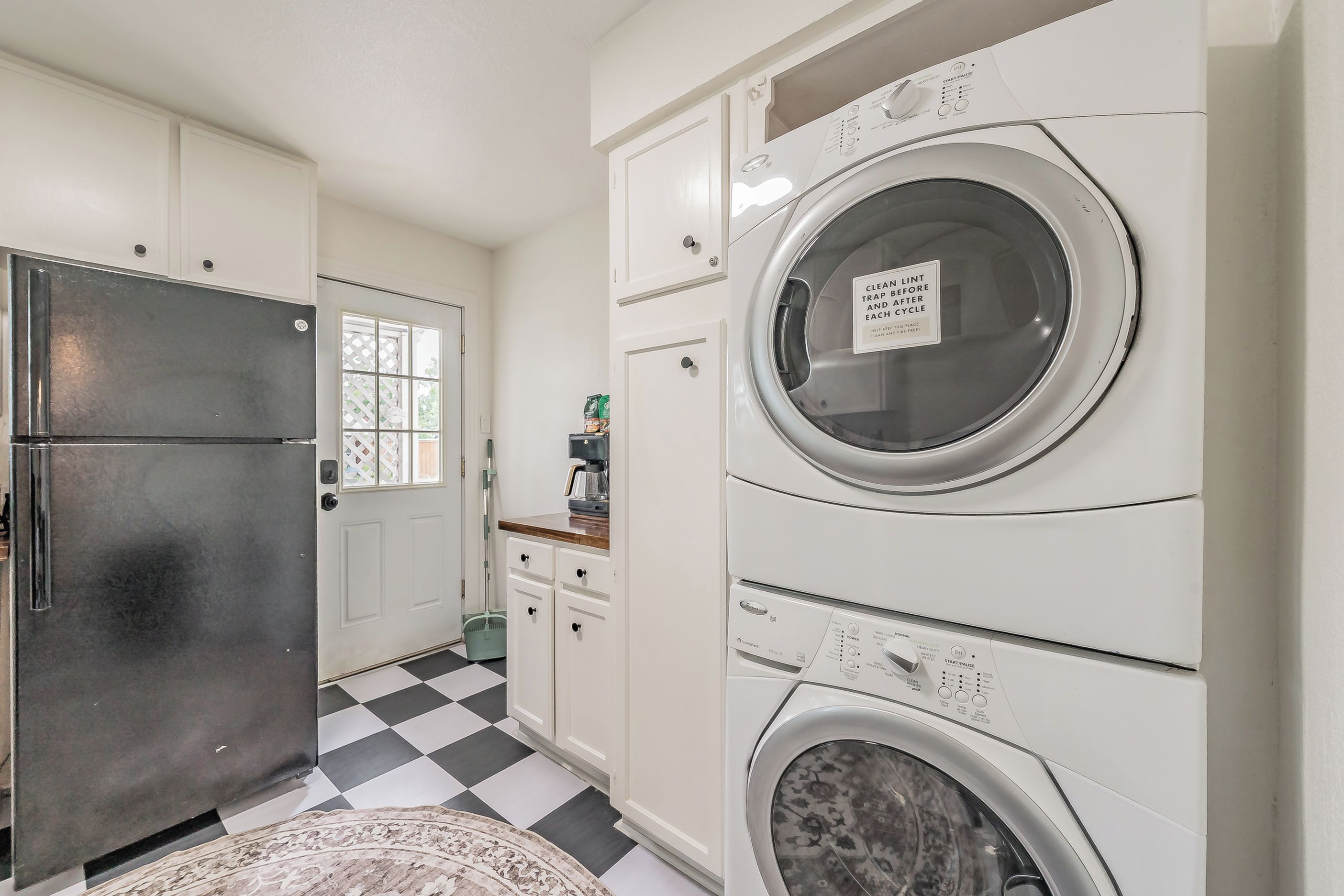 Un espace buanderie équipé d’un lave-linge et d’un sèche-linge à chargement frontal, d’un réfrigérateur et d’une fenêtre ornée d’un motif en treillis.