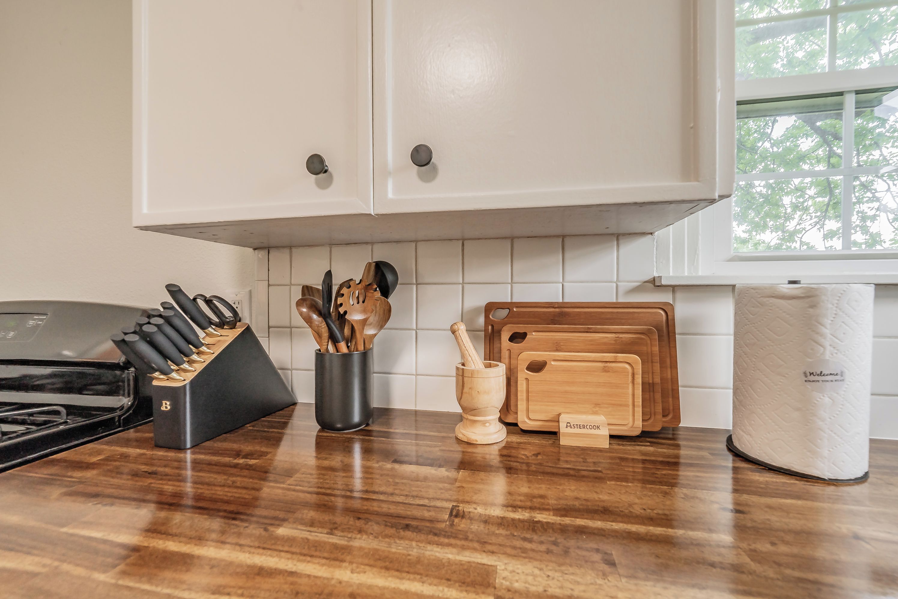 Une cuisine avec des armoires en bois, un bloc à couteaux, des ustensiles de cuisine en bois, un ensemble de planches à découper et un rouleau d’essuie-tout.