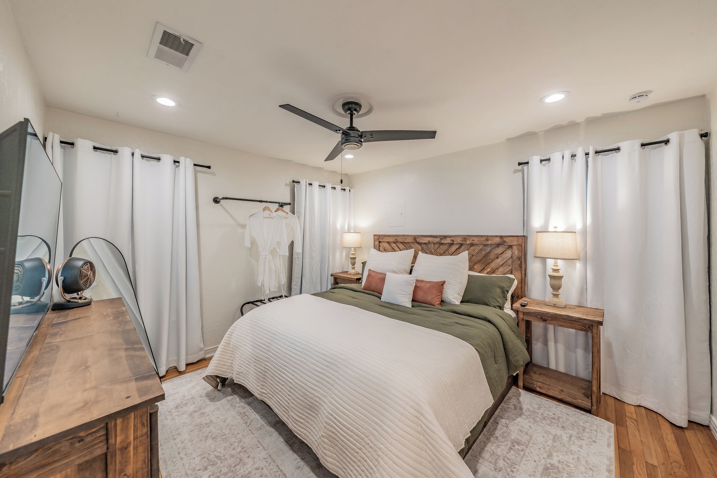 A bedroom with a bed, two bedside tables, a ceiling fan, and a wooden headboard.