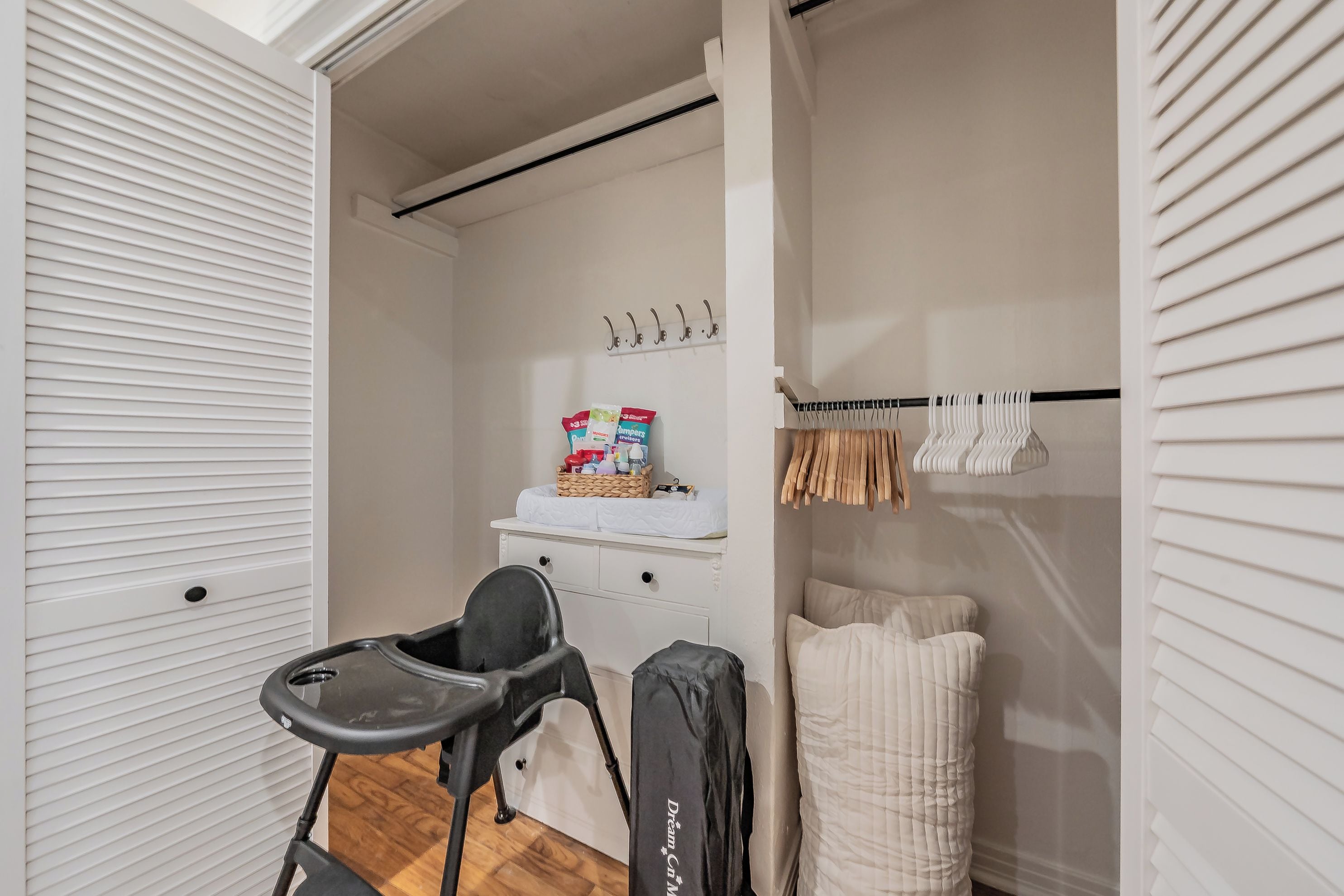 Quarto compacto com um armário branco, carrinho de bebê, berço e prateleira com produtos para bebês.