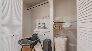 Quarto compacto com um armário branco, carrinho de bebê, berço e prateleira com produtos para bebês.