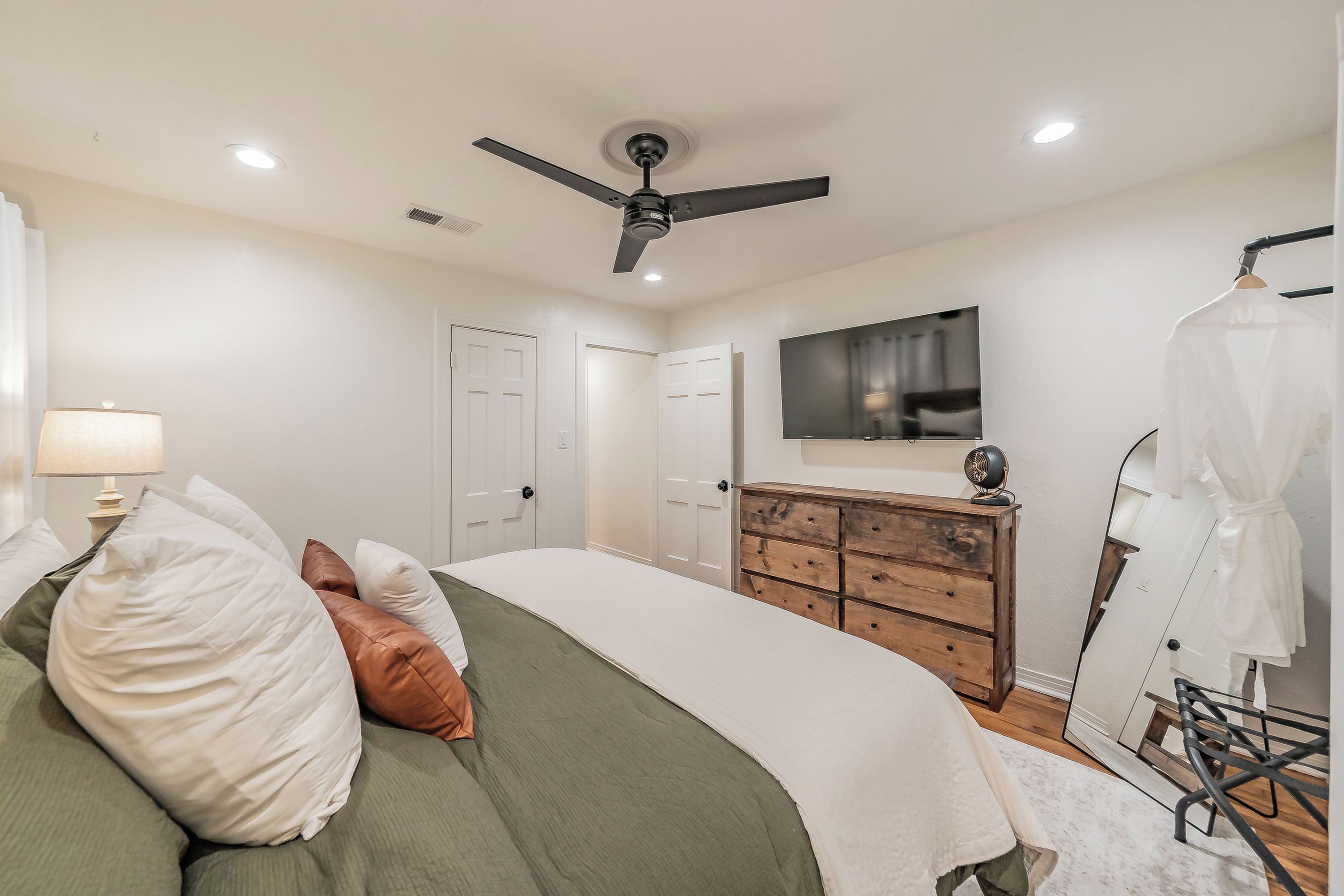 Une chambre à coucher comprenant un lit, une commode, un ventilateur de plafond, un téléviseur et un miroir.