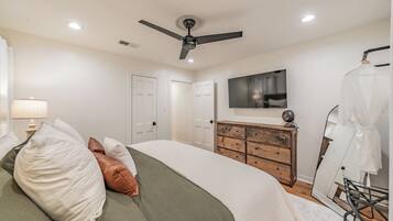 Une chambre à coucher comprenant un lit, une commode, un ventilateur de plafond, un téléviseur et un miroir.