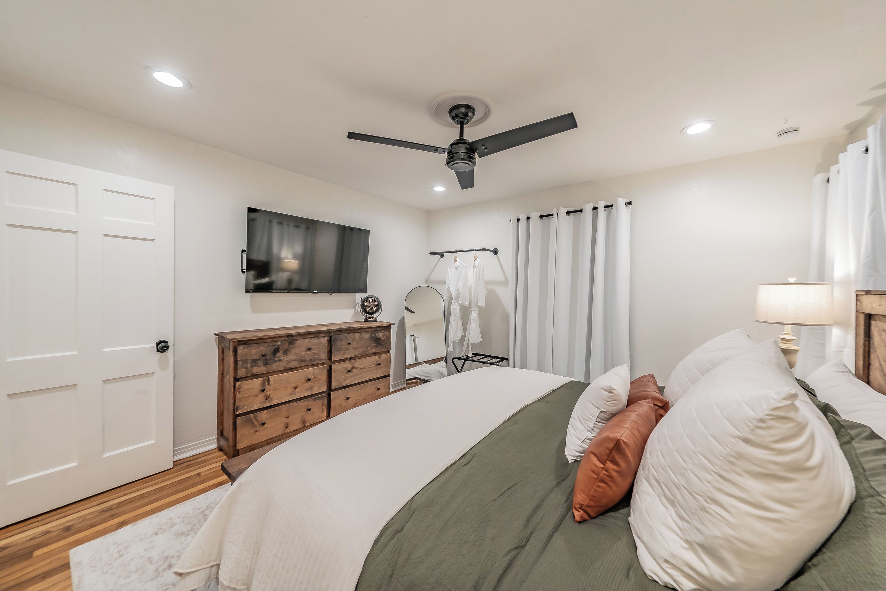A bedroom with a bed, dresser, mirror, and a ceiling fan.