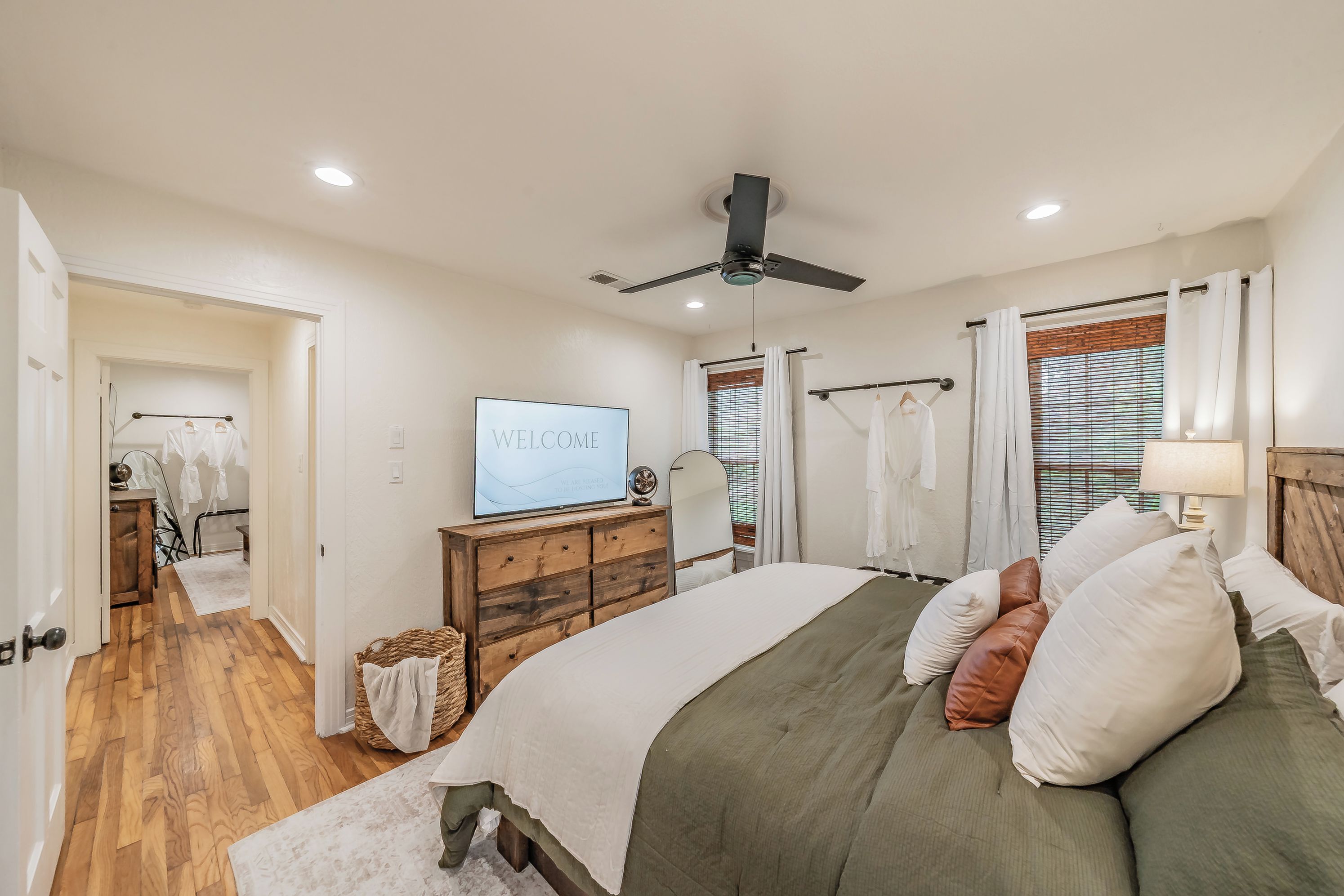 A bedroom with a bed, a television, a ceiling fan, and a window with blinds.
