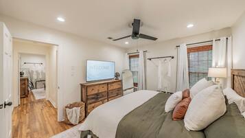A bedroom with a bed, a television, a ceiling fan, and a window with blinds.