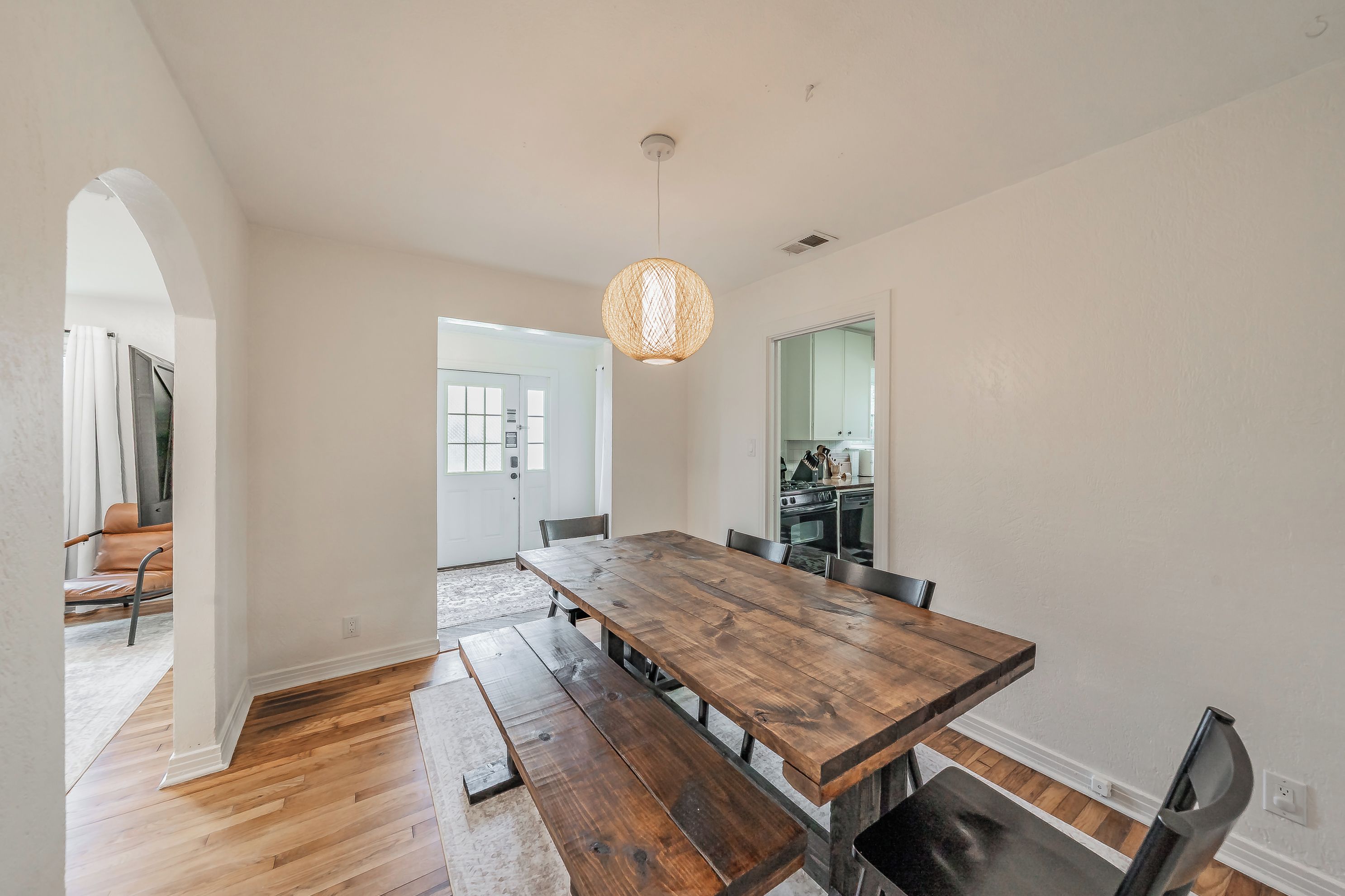Un espace repas avec une table et des bancs en bois, un luminaire suspendu et une vue sur la cuisine.