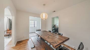 Un espace repas avec une table et des bancs en bois, un luminaire suspendu et une vue sur la cuisine.