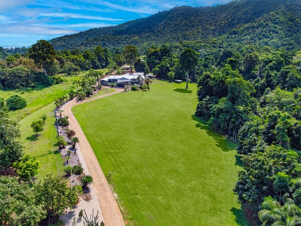 A large, well-maintained lawn with a house surrounded by dense forest.