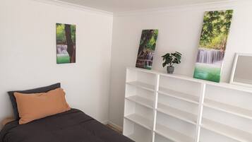 A bedroom with a bed, a white shelving unit, and three wall-mounted paintings.