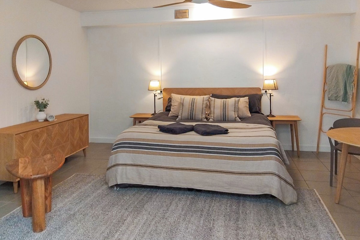 Ein Schlafzimmer mit einem Bett, zwei Nachttischen, einer Holzbank, einem runden Spiegel und einem Deckenventilator.
