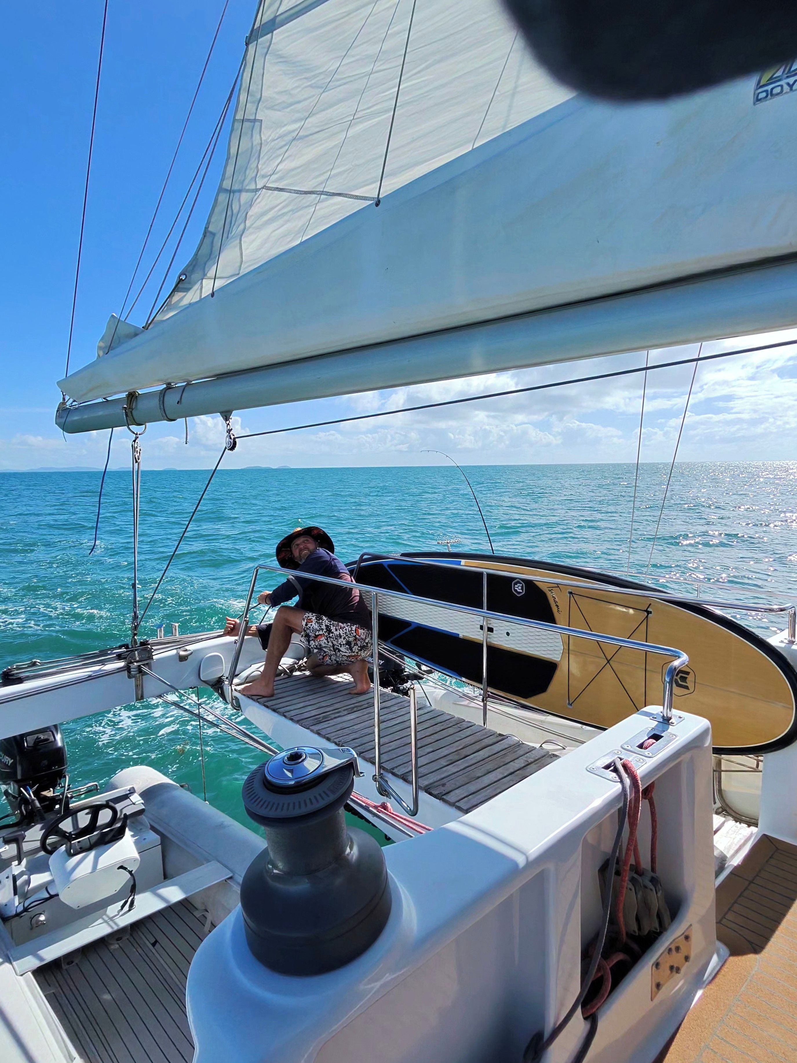 A sailboat with a person on deck, a steering wheel, and a winch.
