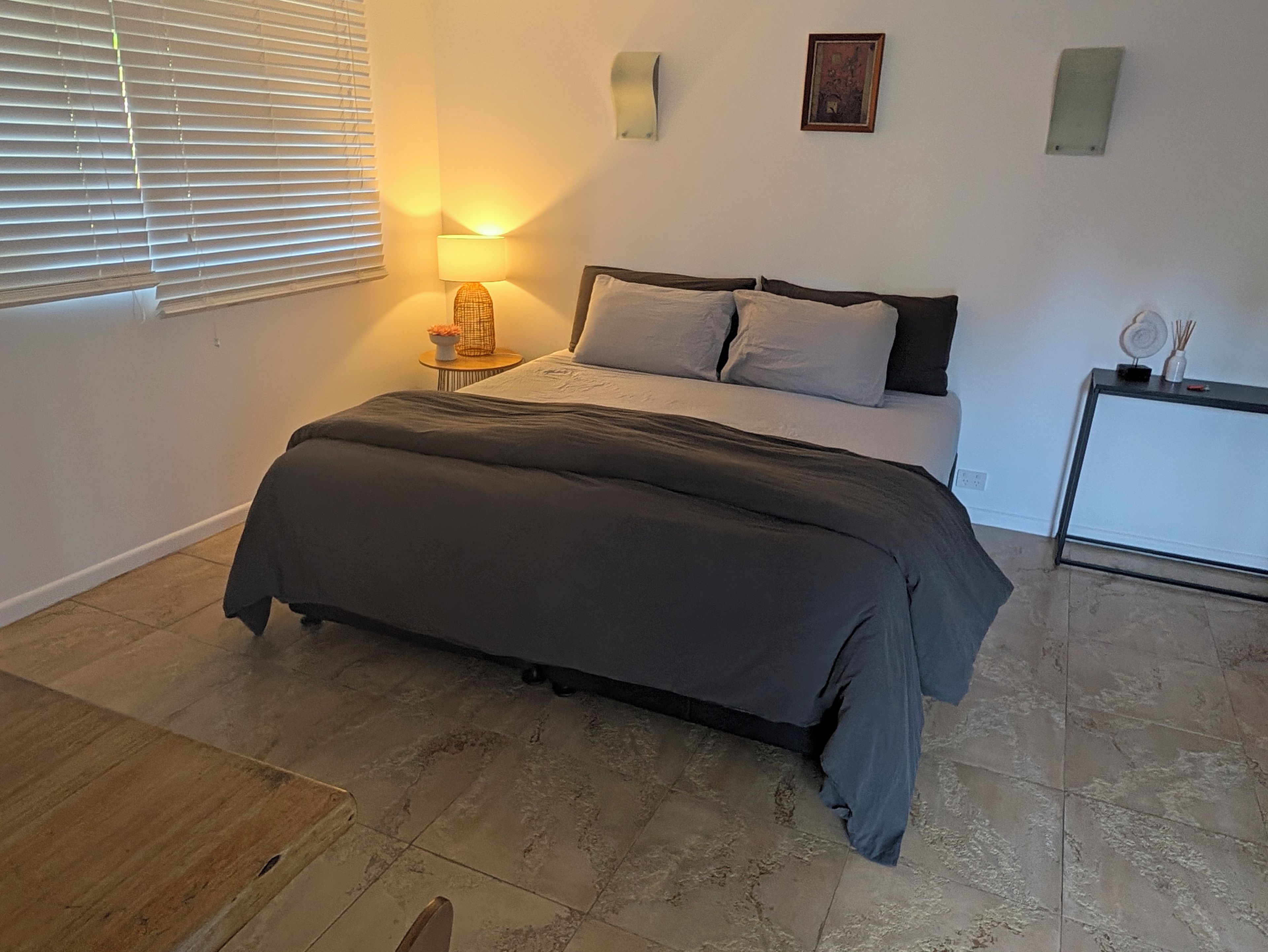 A bedroom with a bed, bedside table, lamp, and a small cabinet.